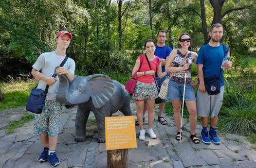 Vanesa so slnečnými okuliarmi v skupinke mladých ľudí pri soche malého slona.