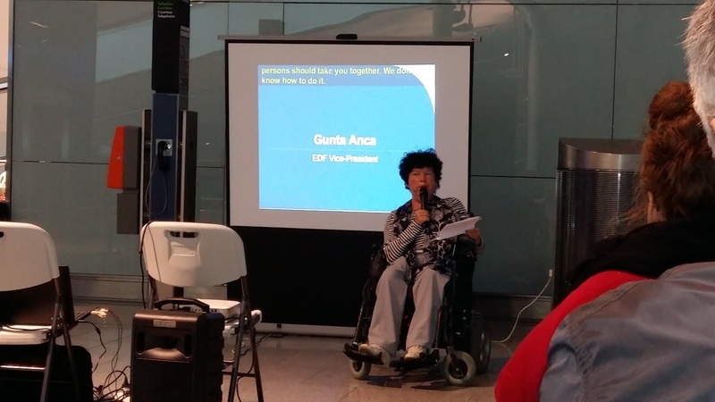 Podpredsedníčka EDF Gunta Anca sedí na invalidnom vozíku pred prezentáciu, v ruke drží mikrofón a papier a rozpráva publiku