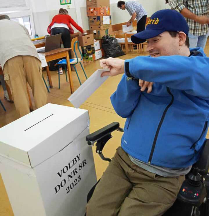 Jozef vo volebnej miestnosti počas volieb do NR SR 2023. V ruke drží obálku, ktorú sa chystá vhodiť do urny.